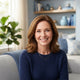 A friendly, diverse woman smiling in a bright, modern living room with soft blue home decor.